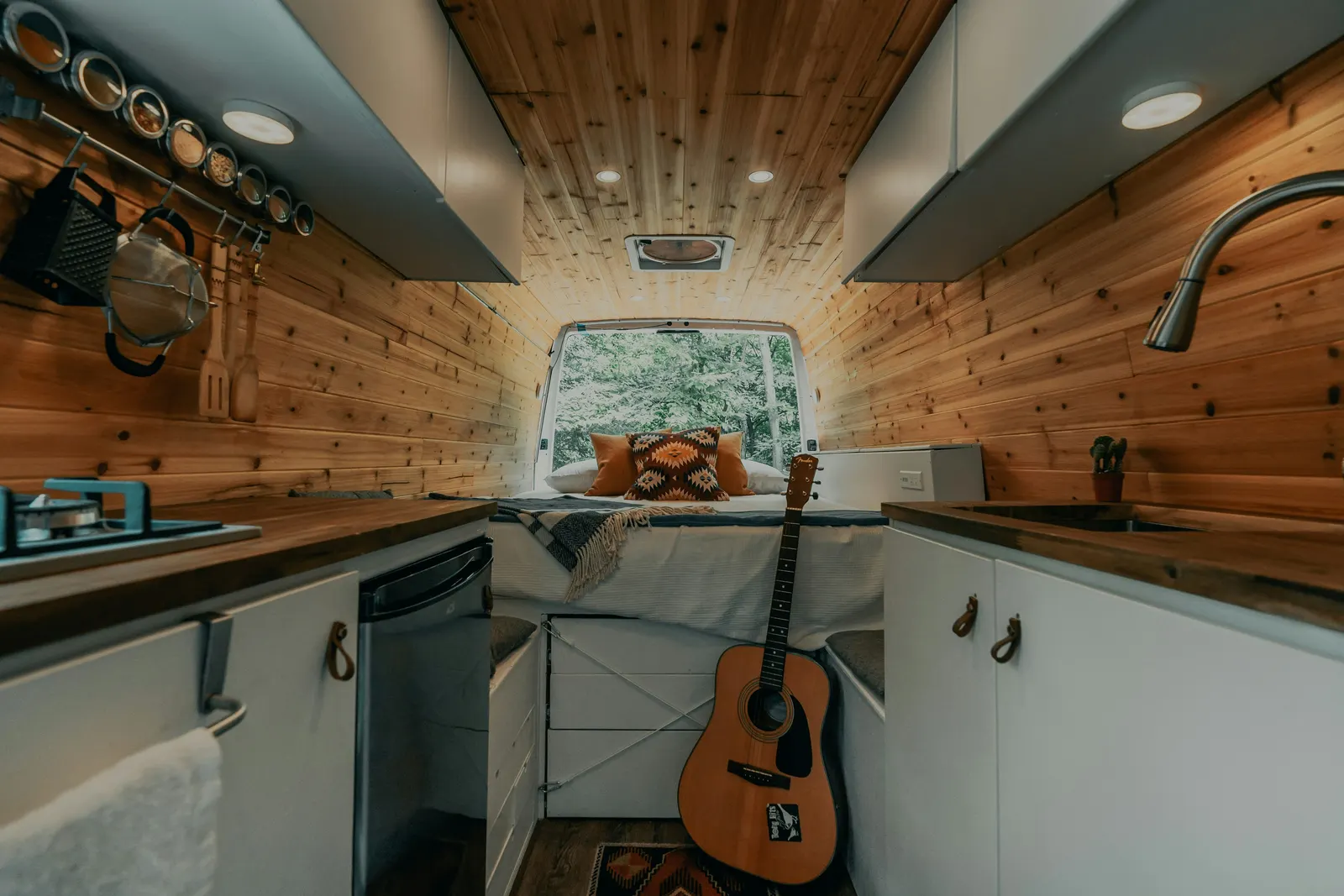 Intérieur d'un fourgon aménagé : cuisine avec plaque gaz et évier, couchage transversal au fond, rangements sous le lit